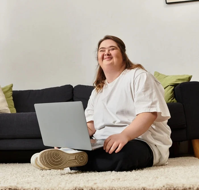 Disabled woman with down syndrome smiling while sitting happily on the ground with laptop