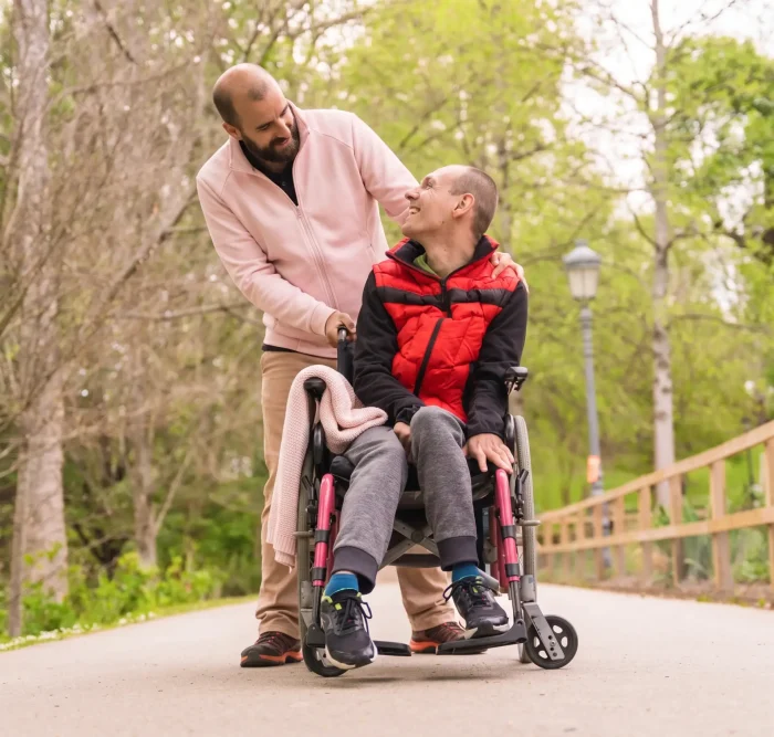 Paralysed young man in a wheelchair being pushed by a friend.